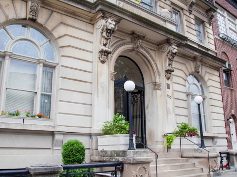 The exterior of an apartment building with potted plants and lion gargoyles on the exterior