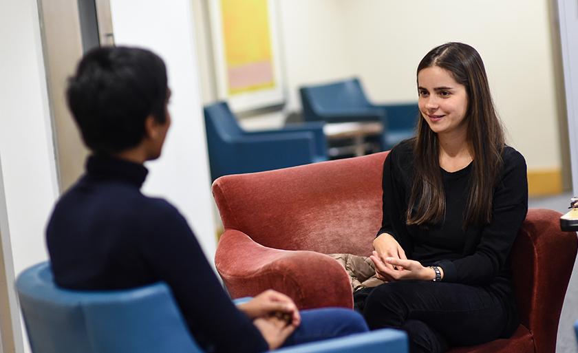 Two women sit in chairs talking to one another.