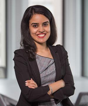 Portrait of Meher Dev smiling with her arms crossed in front of her.
