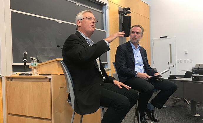 Bruce Sewell speaks in front of a class while seated on a chair, next to Professor Eric Talley.